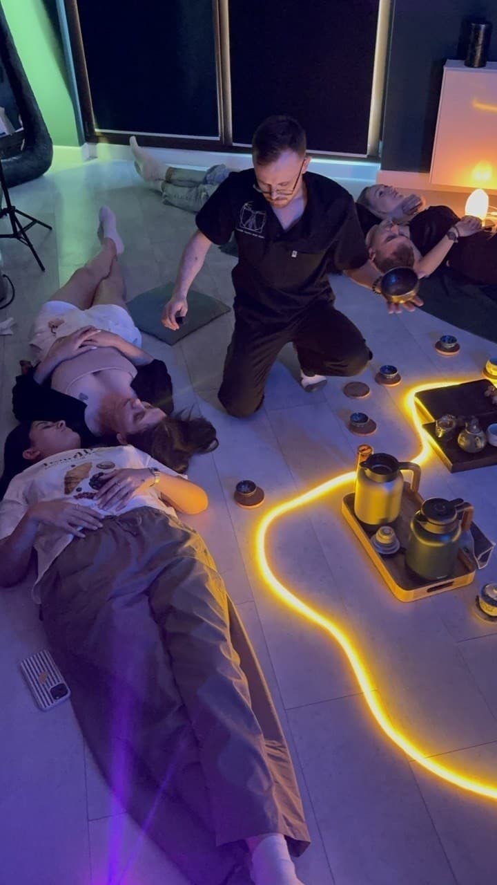 Oleksii with a singing bowl above guests lying on the floor, a tea tray beside them