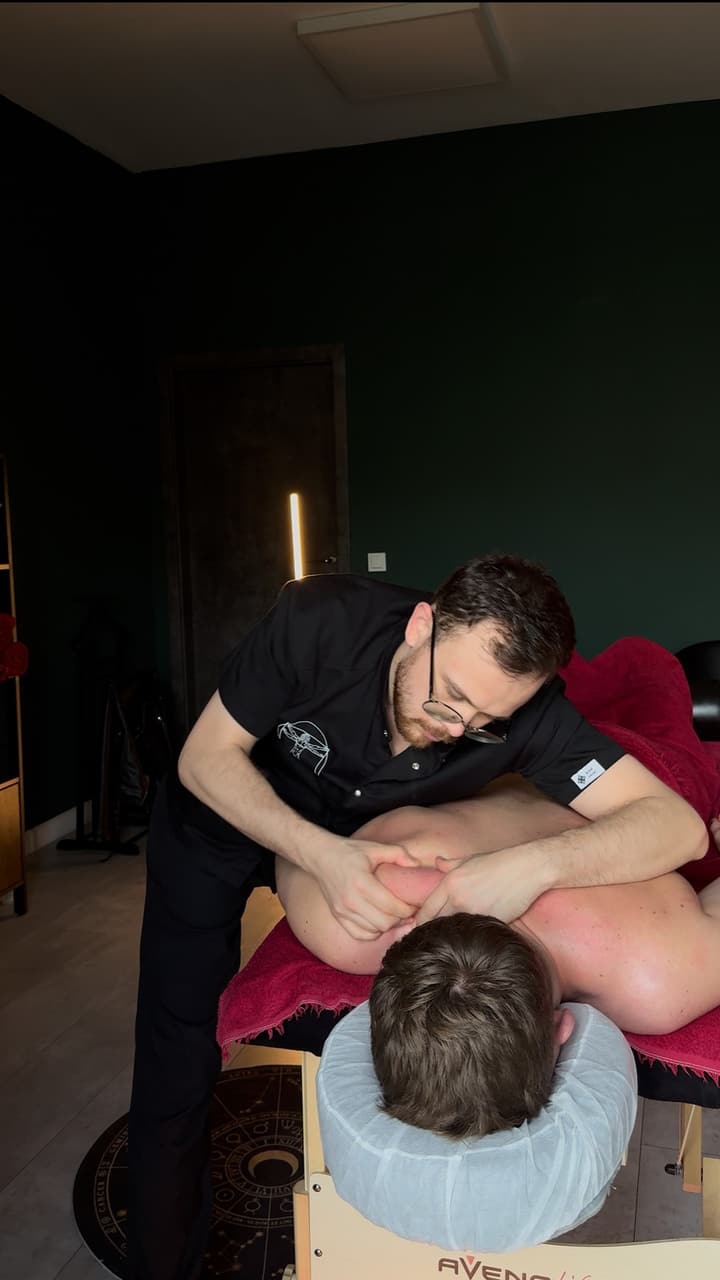 Oleksii working with his hands on the shoulder blade of a client lying on a table with a burgundy towel